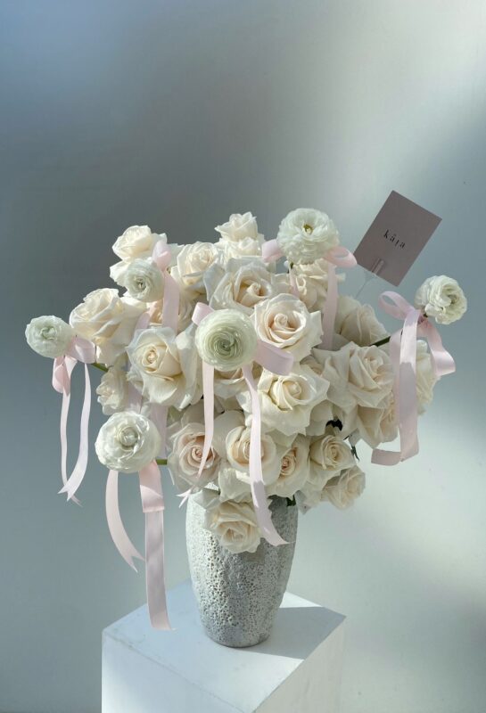 Beautiful bouquet of white and pale pink roses with ribbons in a textured vase, perfect for special occasions or home decor.