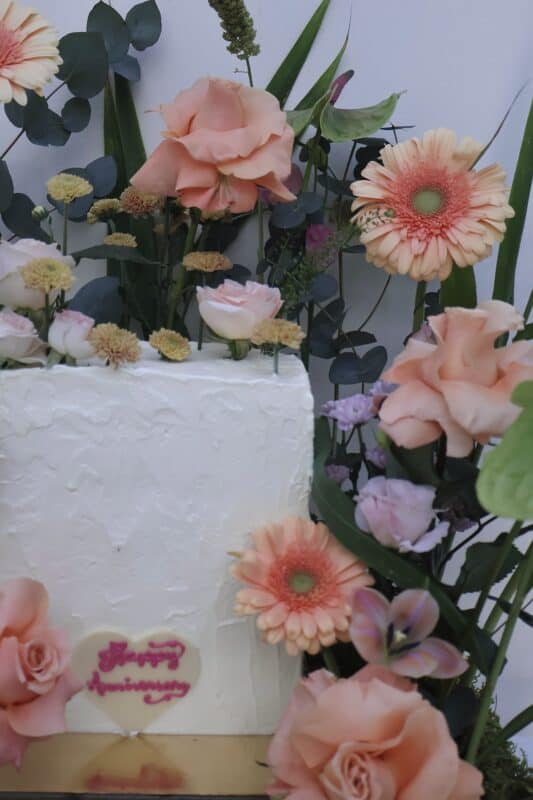 Elegant floral cake decorated with pastel pink roses, gerbera daisies, and greenery, perfect for celebrations.