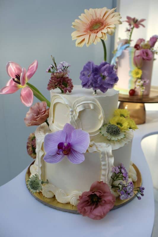 Beautiful wedding cake decorated with a variety of fresh flowers including orchids, daisies, and roses, perfect for a spring or summer celebration.