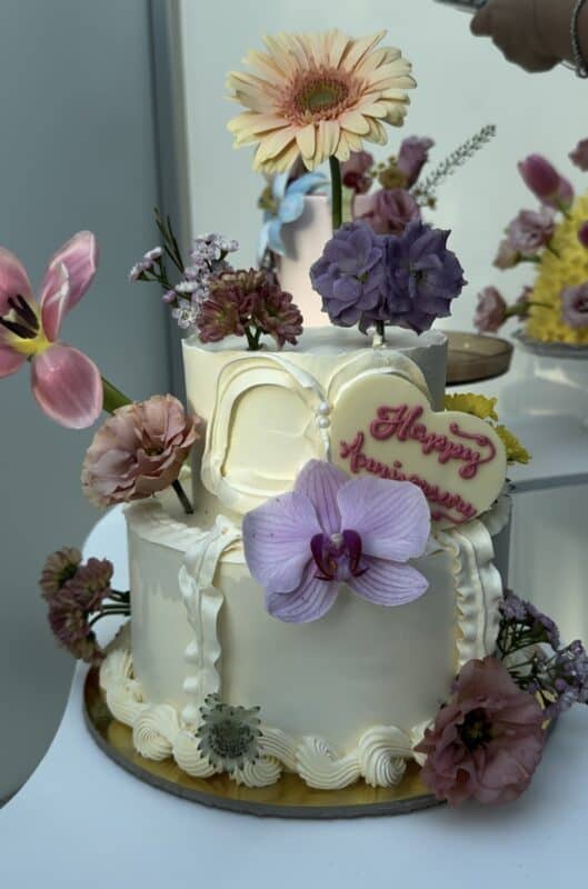 A beautifully decorated celebration cake adorned with fresh flowers including orchids, roses, and lilies, perfect for special occasions.