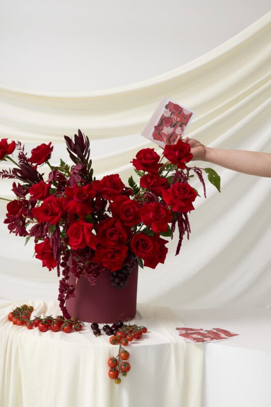 Elegant bouquet of red roses and dark foliage in a deep purple vase, perfect for special occasions or romantic gifts.