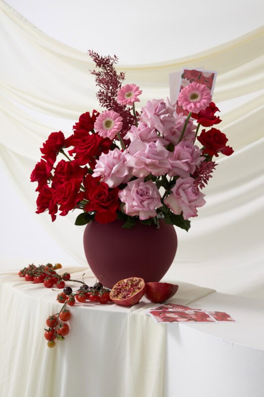 Beautiful pink and red flower bouquet featuring roses and gerbera daisies in a deep burgundy vase, perfect for special occasions or home decor.