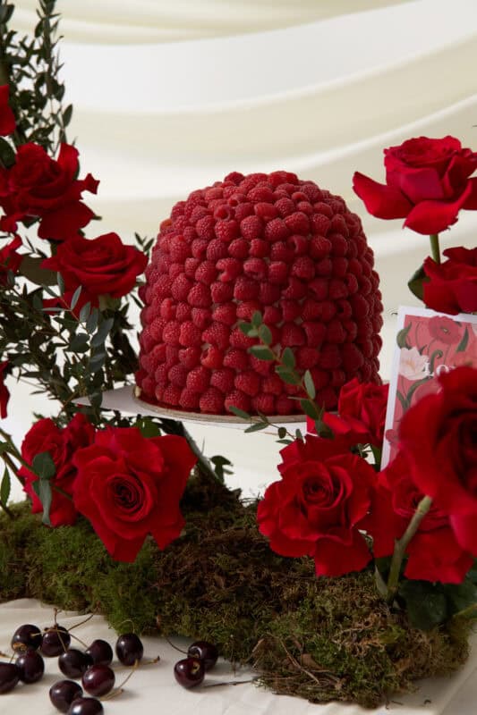 Elegant raspberry floral centerpiece surrounded by red roses and greenery, perfect for special occasions and events.