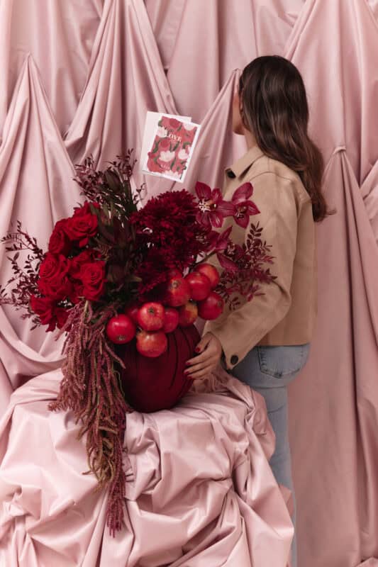 Elegant floral arrangement featuring deep red roses, dahlias, and apples for Garnet No. 9.