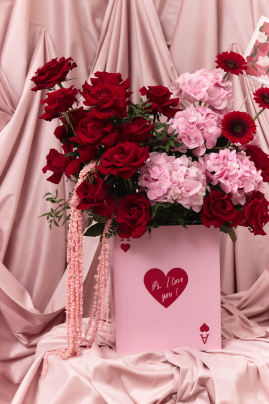 Beautiful floral display featuring red roses, pink hydrangeas, and red gerbera daisies arranged in a pink gift box with a "P.S. I Love You" message. Perfect for romantic occasions and floral gift idea.