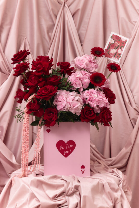 Beautiful Valentine's bouquet featuring red roses, pink hydrangeas, and red gerbera daisies arranged in a pink box with a love message, perfect for romantic occasions.
