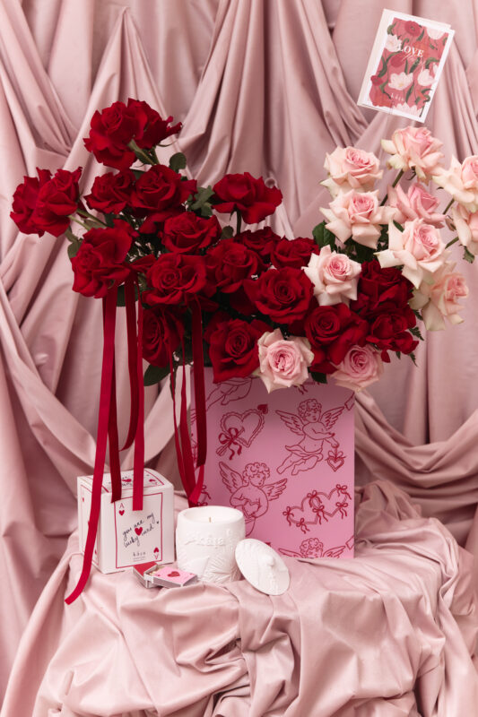 A beautiful arrangement of red and pink roses in a gift box, complemented by candles and decorative items, perfect for romantic occasions or floral gifts.