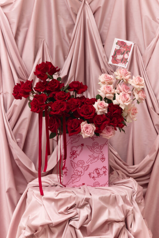 Beautiful red and pink roses arranged in a stylish bouquet, perfect for romantic celebrations, weddings, or gifting. The flowers are displayed against soft pink drapery, enhancing their vibrant colors.