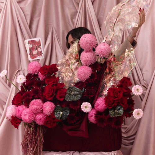 Elegant floral display featuring pink and red roses with dark green foliage, set against soft pink draped fabric for a romantic and dreamy aesthetic.