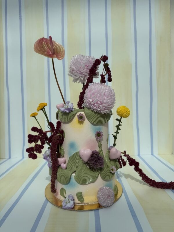 Elegant floral cake featuring pink, purple, and yellow flowers with green foliage, perfect for special occasions and celebrations.