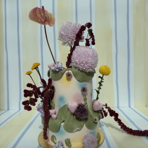 Elegant floral cake featuring pink, purple, and yellow flowers with green foliage, perfect for special occasions and celebrations.
