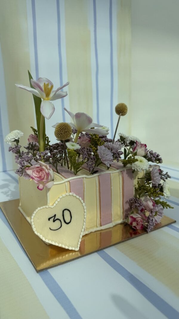 Elegant floral cake decorated with pink roses, white lilies, and assorted fresh flowers for special occasions.