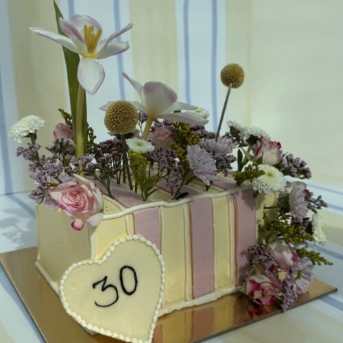 Elegant floral cake decorated with pink roses, white lilies, and assorted fresh flowers for special occasions.