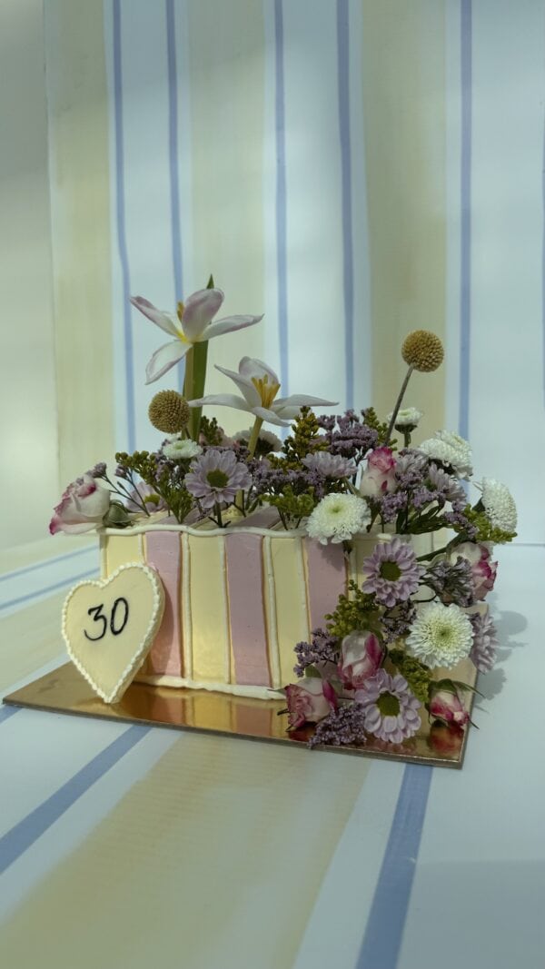 Beautiful floral cake decorated with fresh flowers including orchids, daisies, and roses in pastel shades, perfect for celebrations and special occasions.