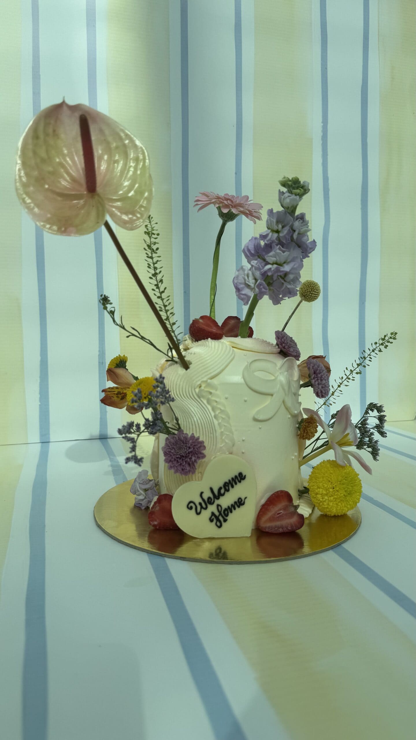 Elegant floral cake decorated with fresh flowers and fruits, featuring a large anthurium, roses, and other blooms, perfect for celebrations.