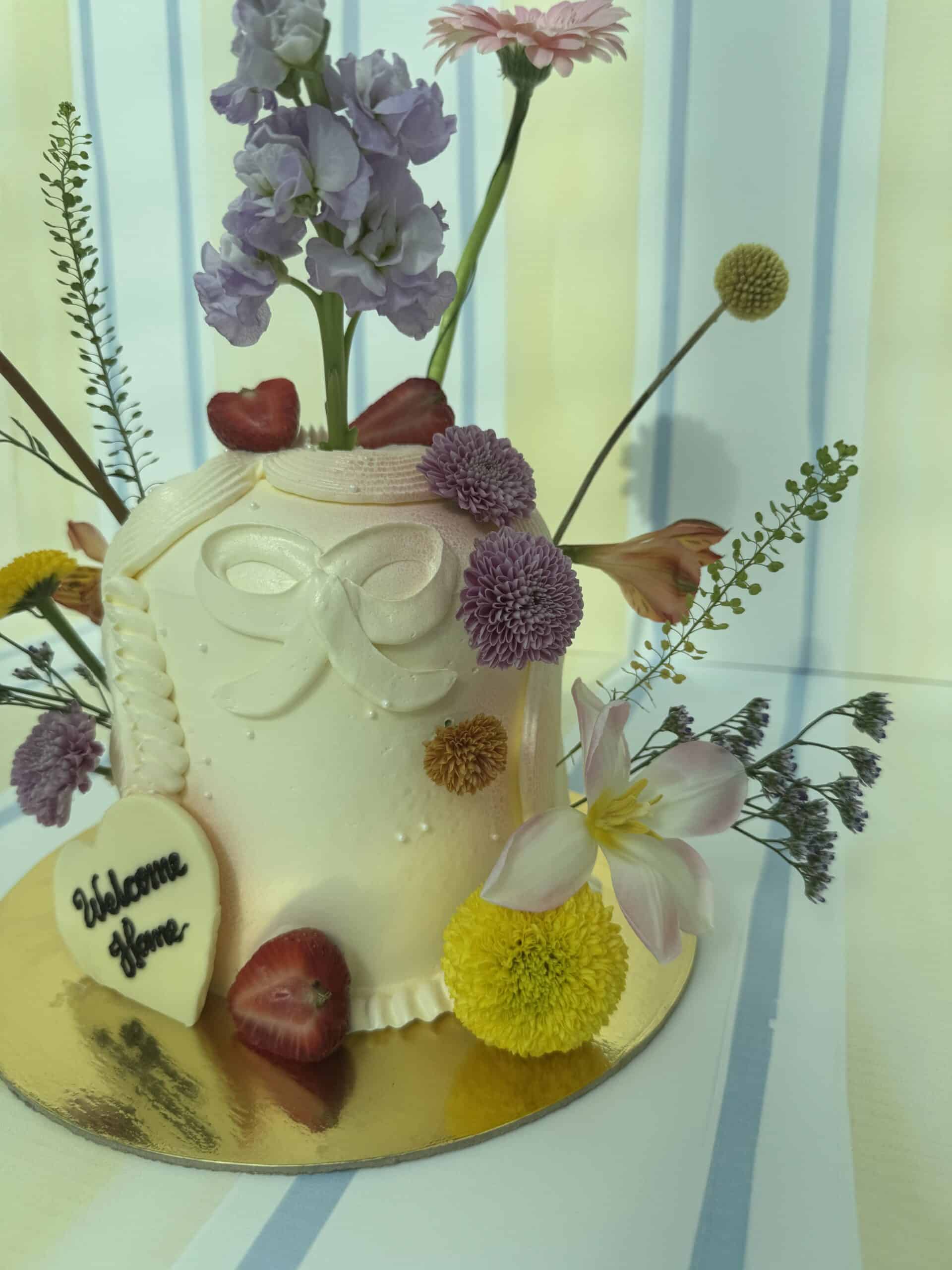 Elegant floral cake decorated with fresh flowers including lilies, daisies, and purple alliums, perfect for celebrations.
