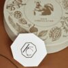 Elegant round gift box with botanical illustrations and a central squirrel logo, labeled Kaia Chocolatier, perfect for chocolate floral gift presentation.