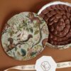 Elegant round gift box filled with chocolate ovals, featuring a nature-inspired design with squirrels and leaves, perfect for gifting.