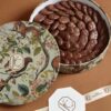 Elegant round gift box filled with glossy chocolate ovals, decorated with a floral and animal print lid, perfect for gifting or indulgence.