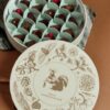 Elegant round chocolate box with assorted chocolates and berries, featuring a botanical design on the lid, perfect for gifting or special occasions.
