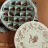 Elegant round box of assorted chocolates with floral and nature-inspired illustrations on the lid, featuring a squirrel and botanical elements, perfect for gift-giving.