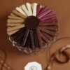 Assorted chocolate bird sticks arranged in a circular pattern on a glass cake stand, featuring various flavors and colors for dessert decoration.